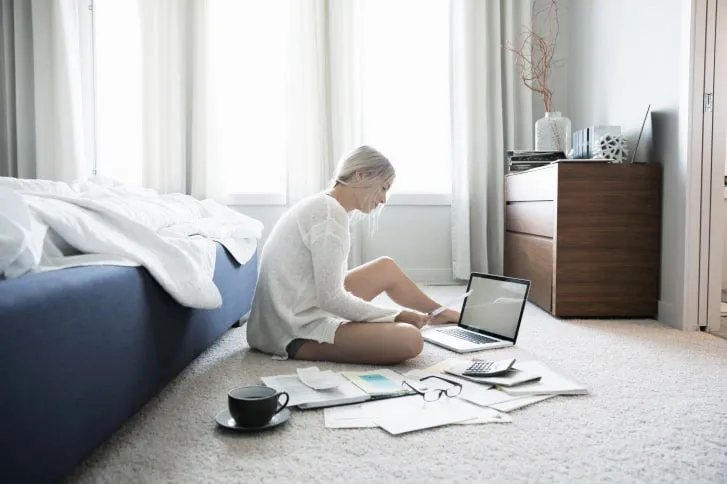 Woman paying bills at laptop on bedroom floor