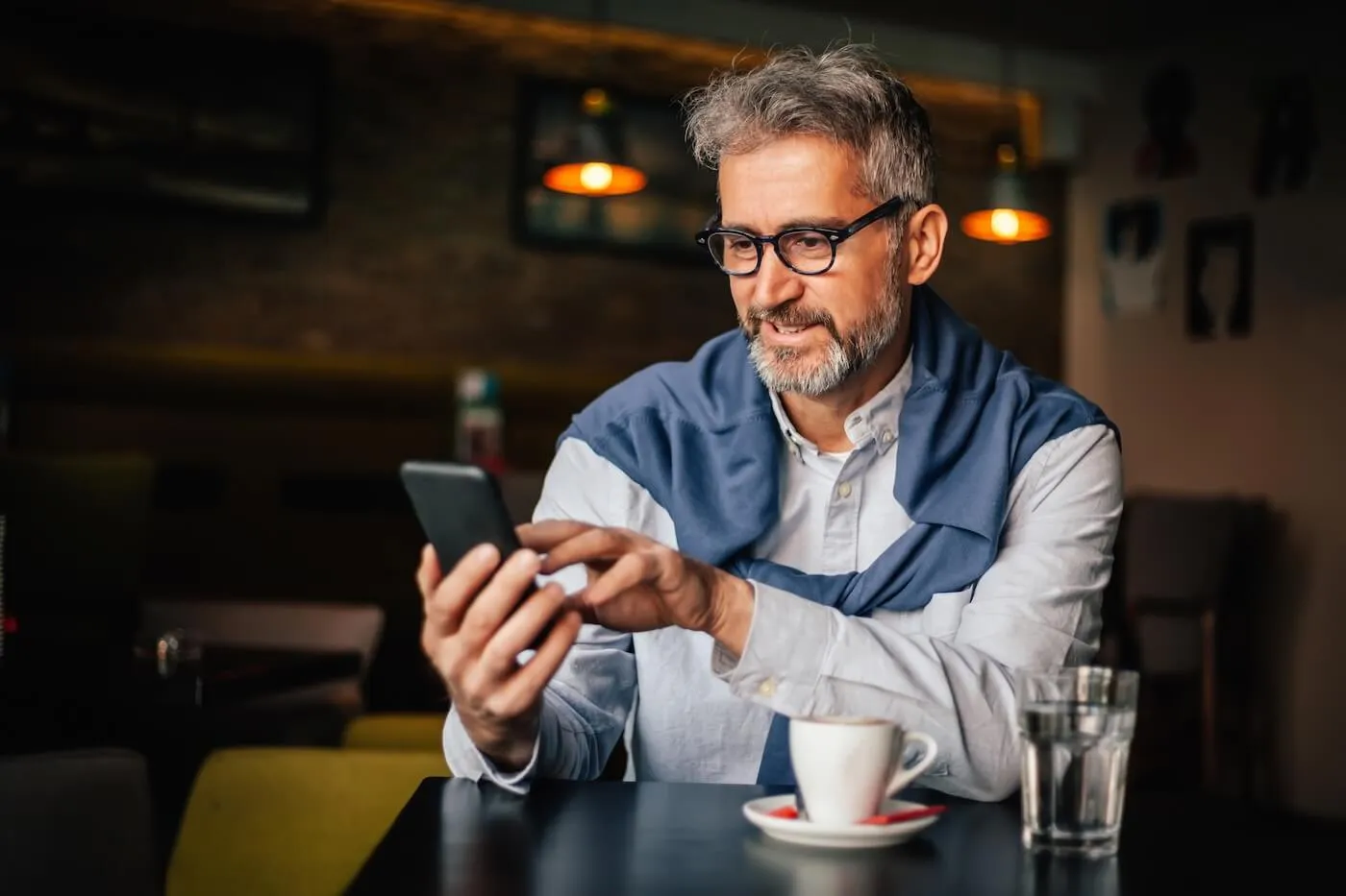 Smiling mature man enjoying espresso in the cafe and checking his mobile phone