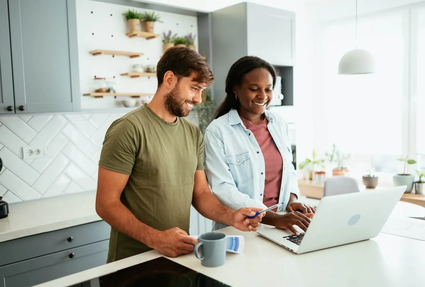 Happy young couple using a laptop in the kitchen while having a hot drink