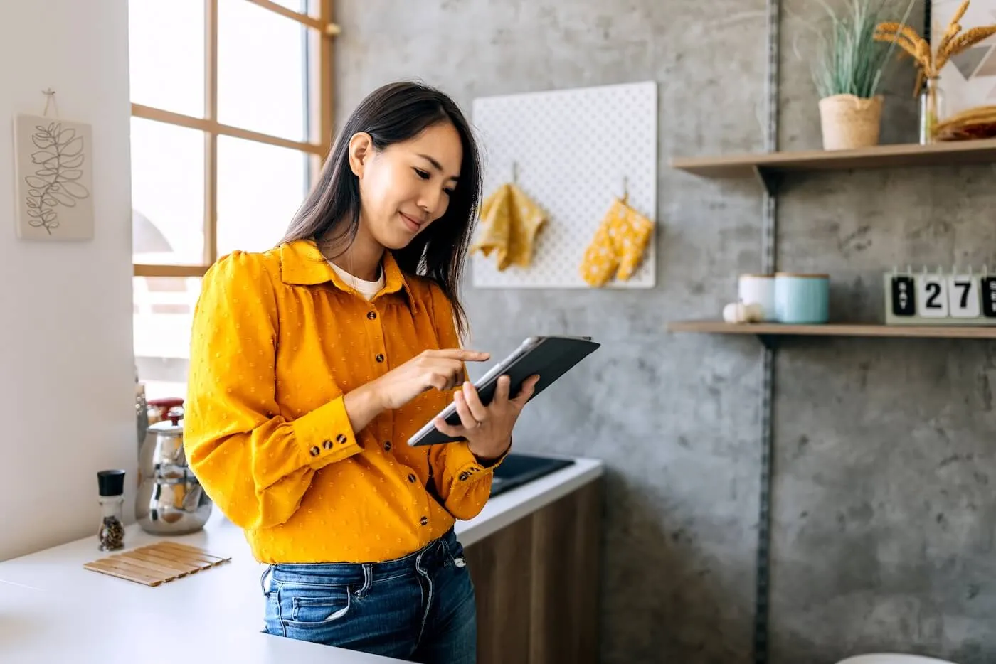 Smiling young woman standing in the kitchen checking her CD account on the tablet