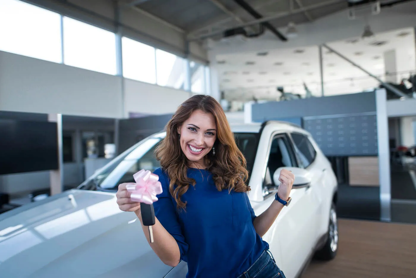 Smiling young woman standing in front of the white car and holding the car keys with a bow