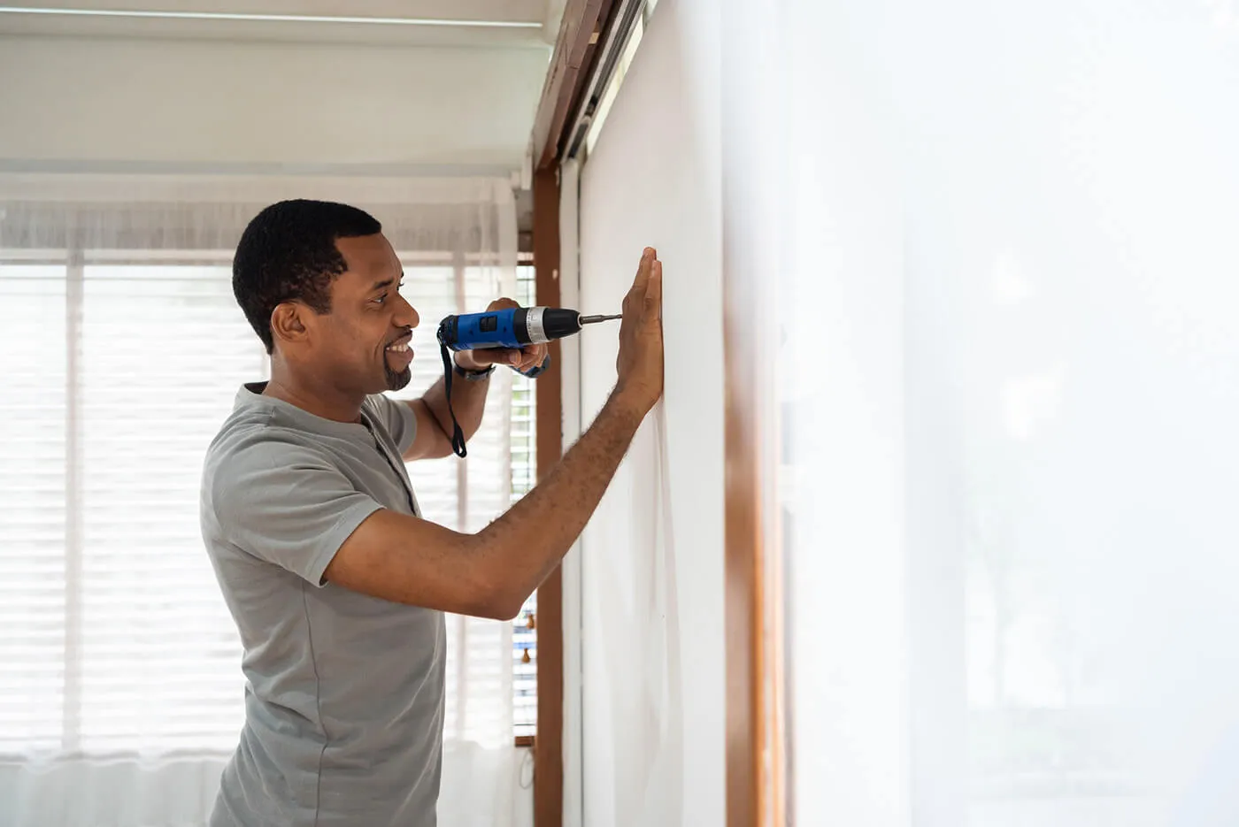 Smiling man using electric drill on the wall