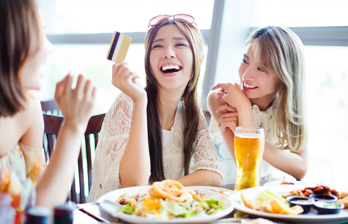 Three happy female friends enjoy a meal at a café, with one of them holding a credit card