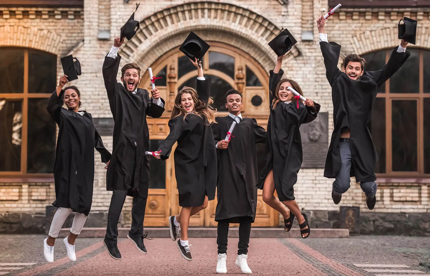 A cheerful group of college graduates jumping in the air, holding their graduation caps in their hands, celebrating together outdoors
