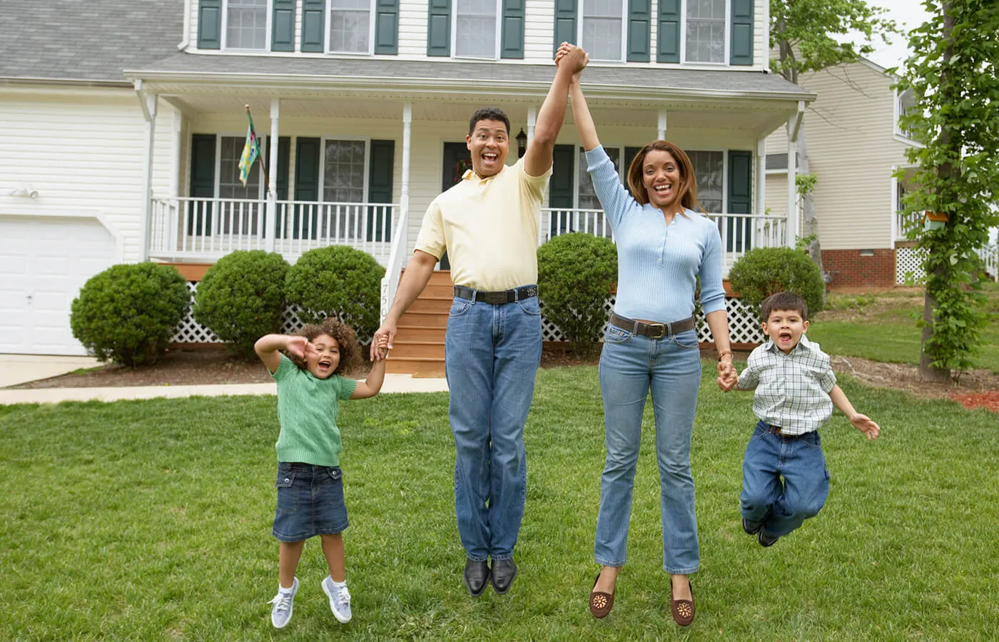 Happy family of four holding hands and jumping in the air on the front yard of their house
