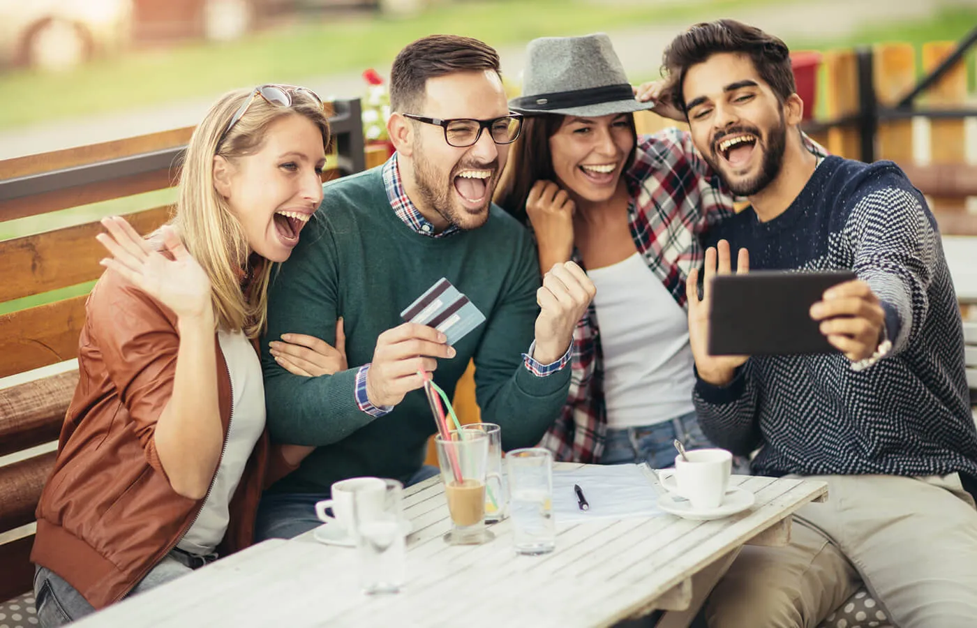 A cheerful group taking a selfie in a café, with one man holding credit cards