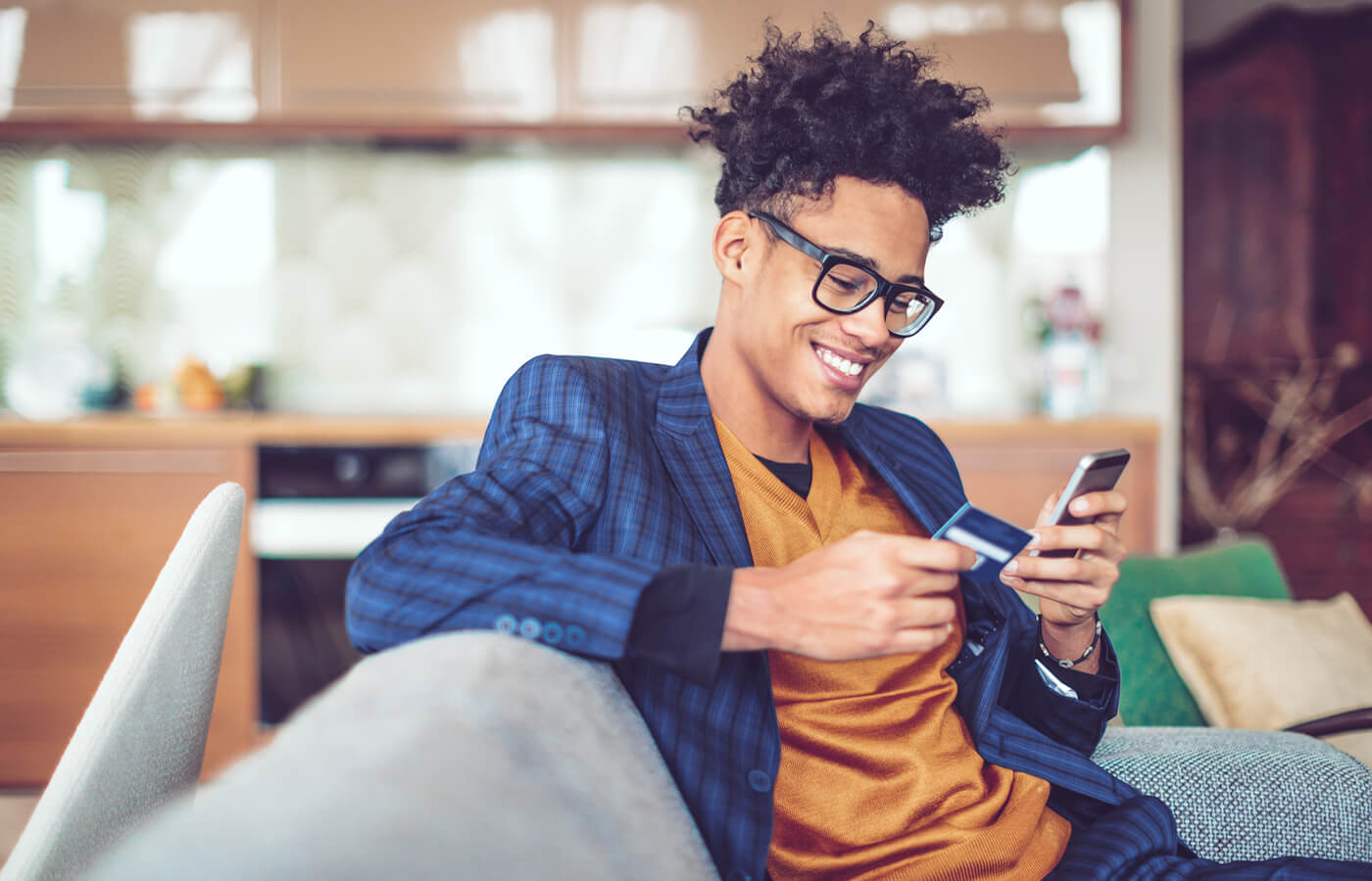 Smiling young man using his credit card and a smartphone at home