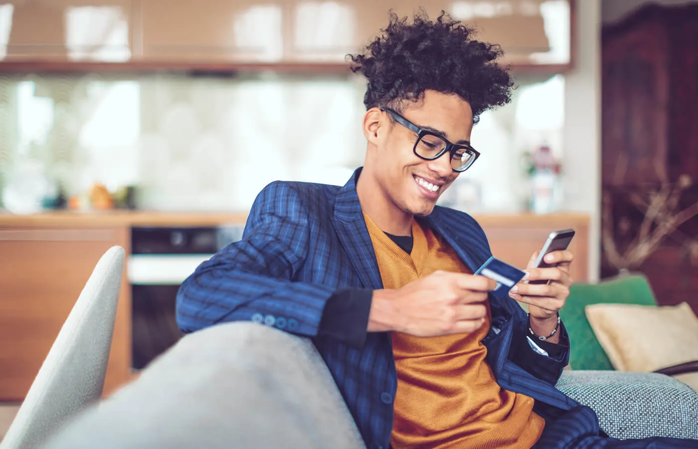 Smiling young man using his credit card and a smartphone at home