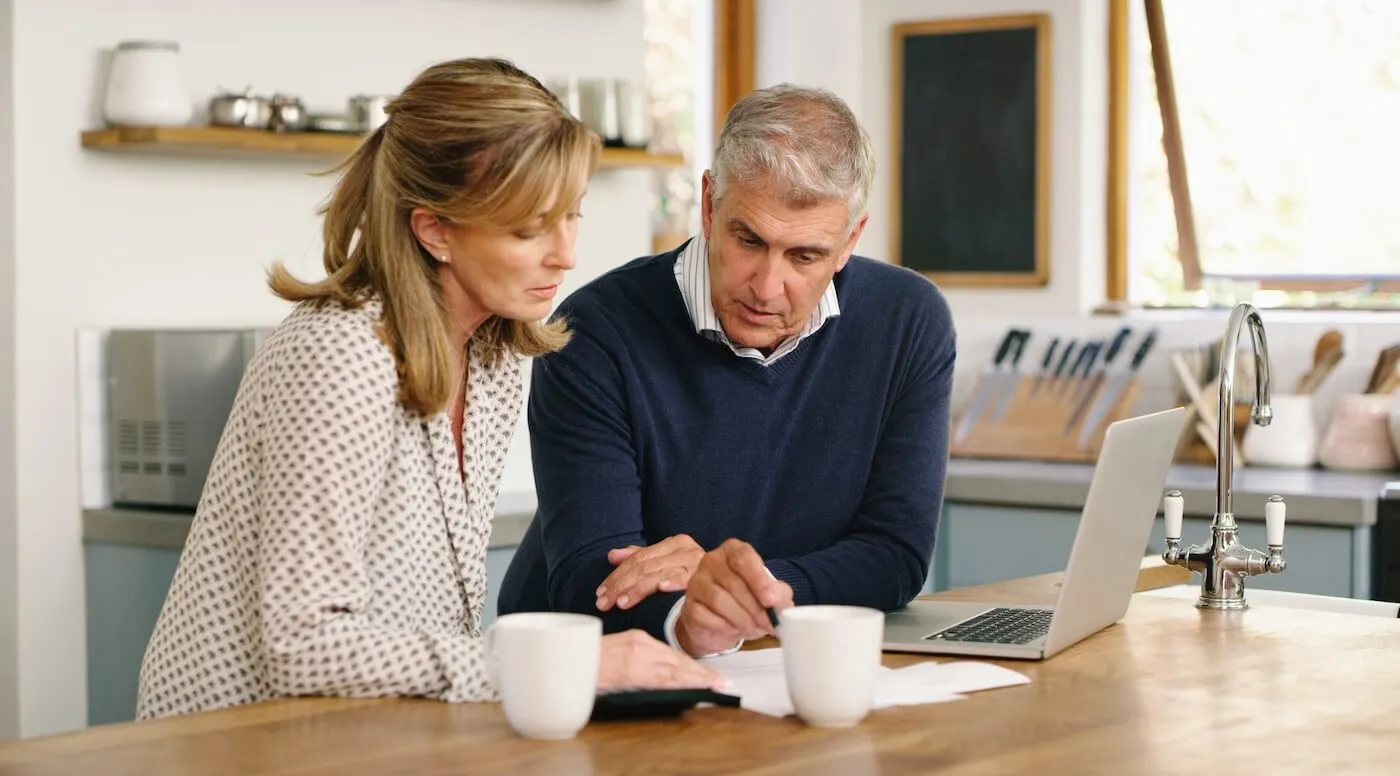 A senior couple planning their finances while using a laptop at home.