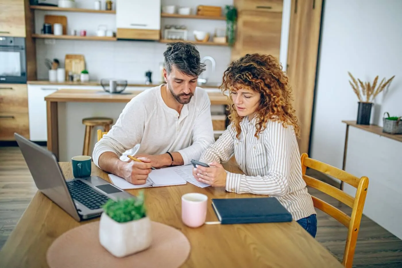 Focused couple planning their finances in the kitchen, using a laptop and making notes