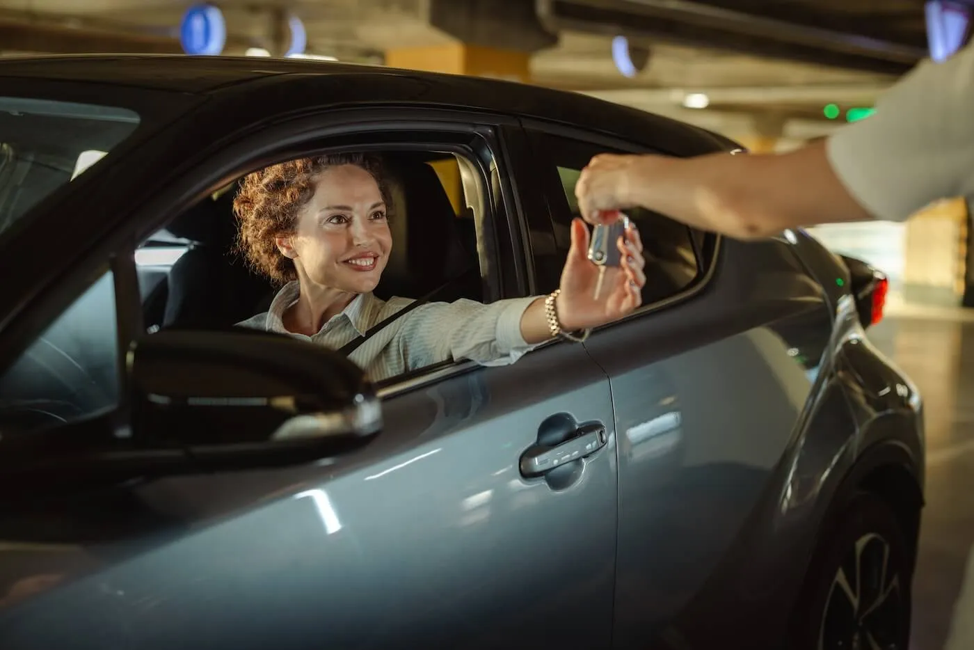 Smiling mature woman sitting in the car and taking the car keys from another person through the open window