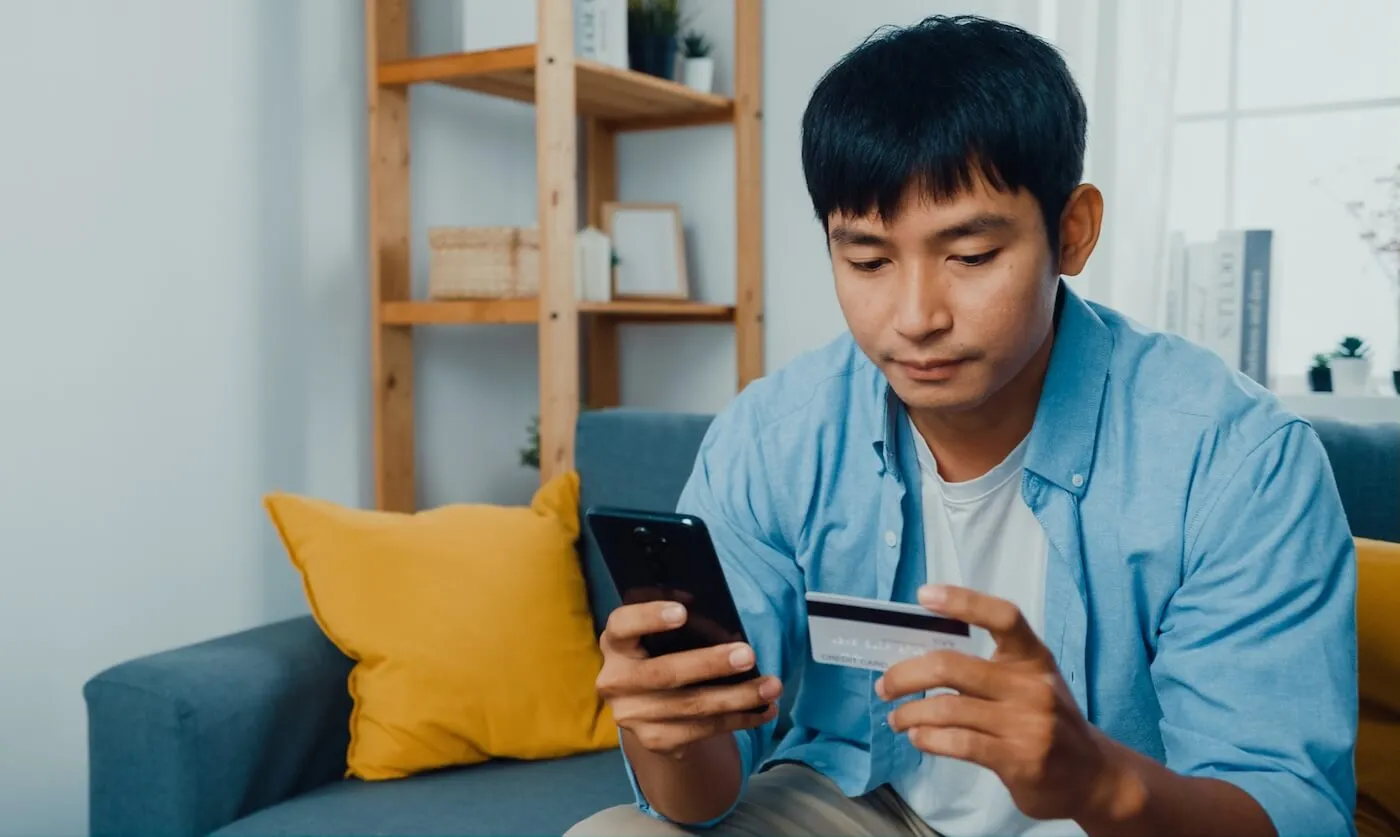 Focused young man sitting on a sofa with a smartphone and a credit card