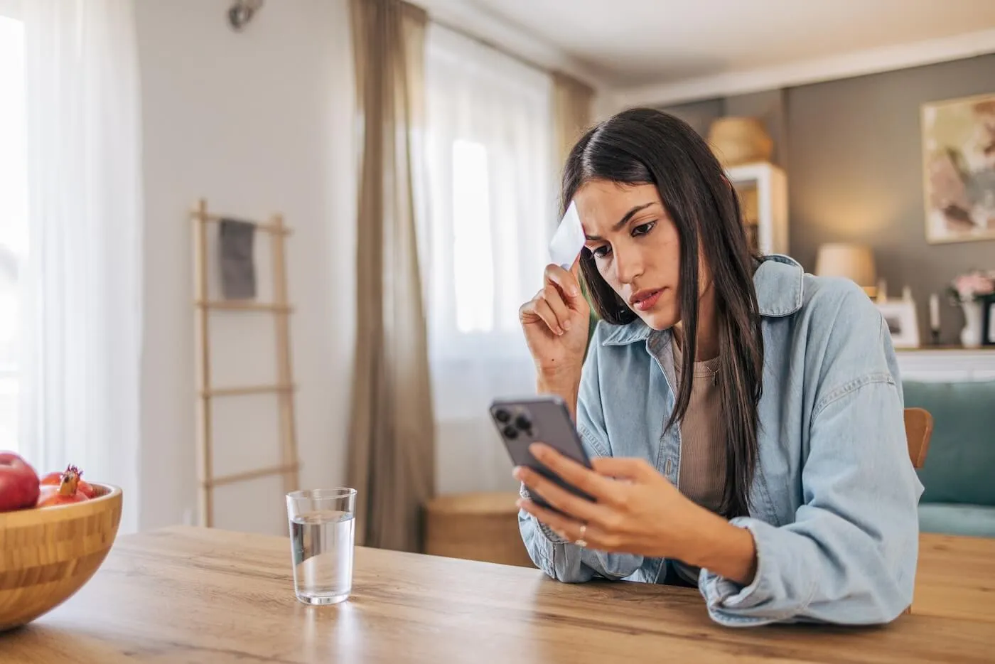 Concerned young woman holding a credit card while checking her bank account on the smartphone