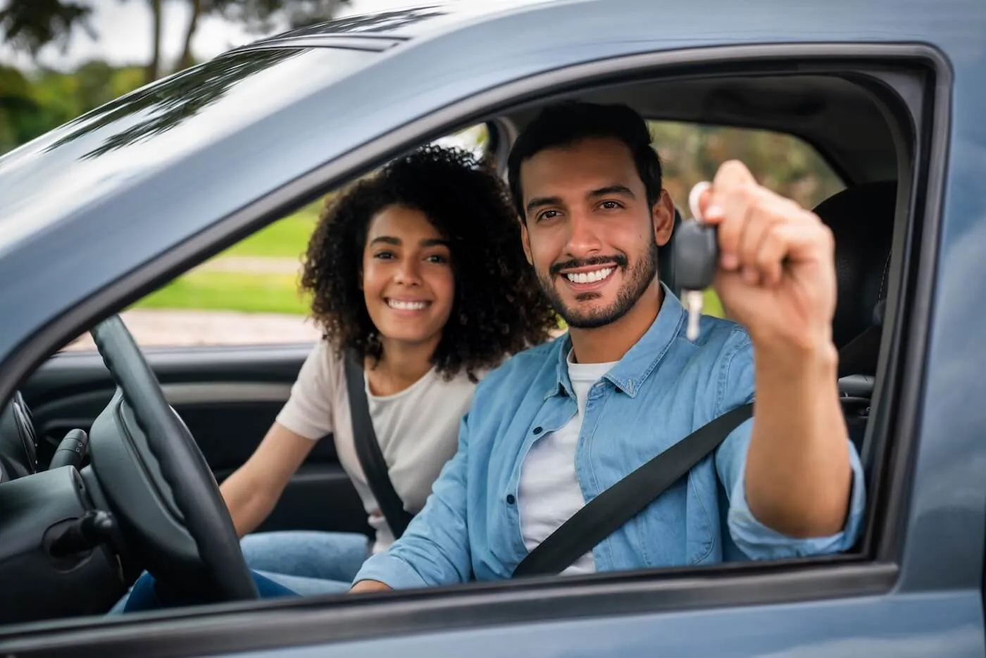 Happy young couple sitting in the car, the man is holding the car keys