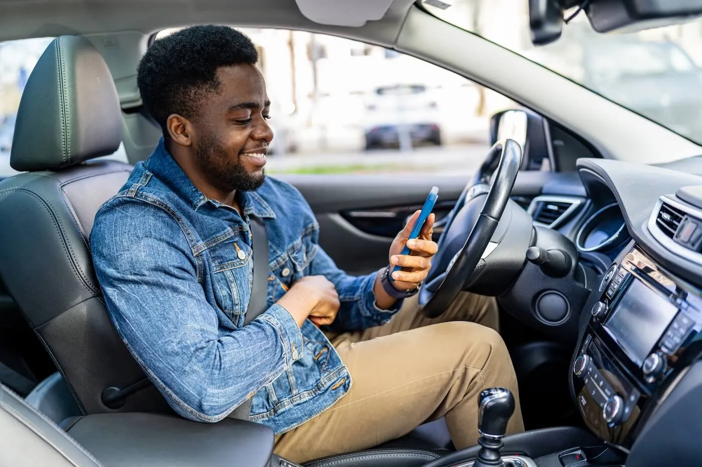 Smiling young man checking his smartphone in a parked car