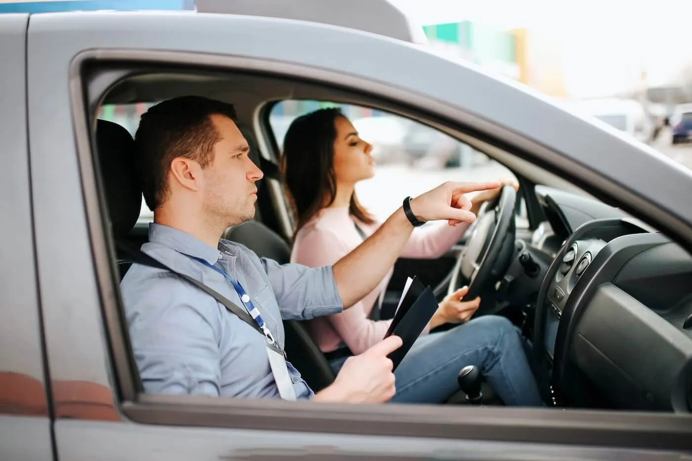 Male auto instructor is pointing the direction to a young woman who is taking a driving test
