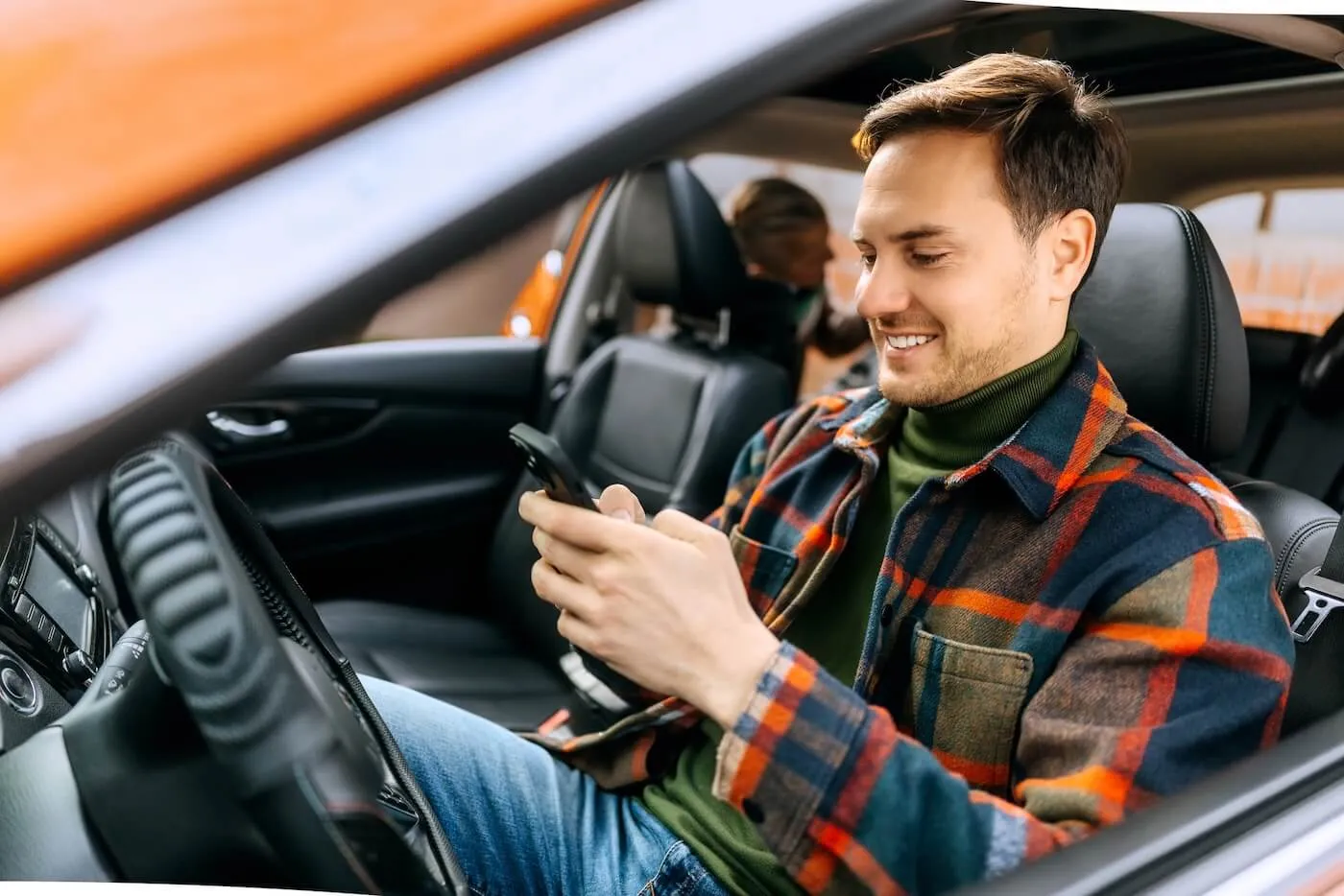 Smiling man checking his smartphone in the parked car