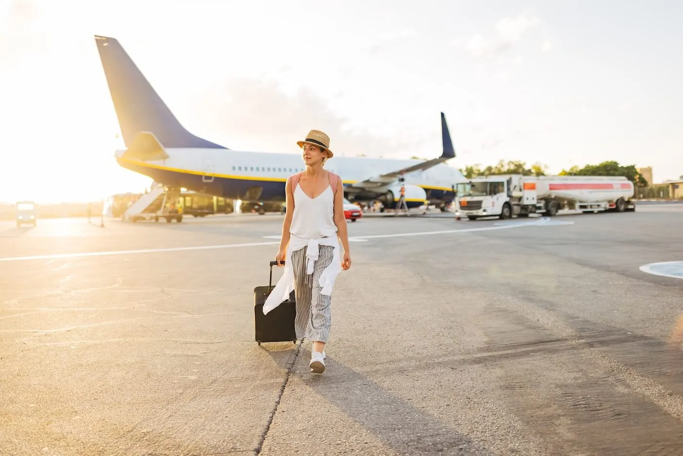 Young woman with a suitcase walking away from the airplane
