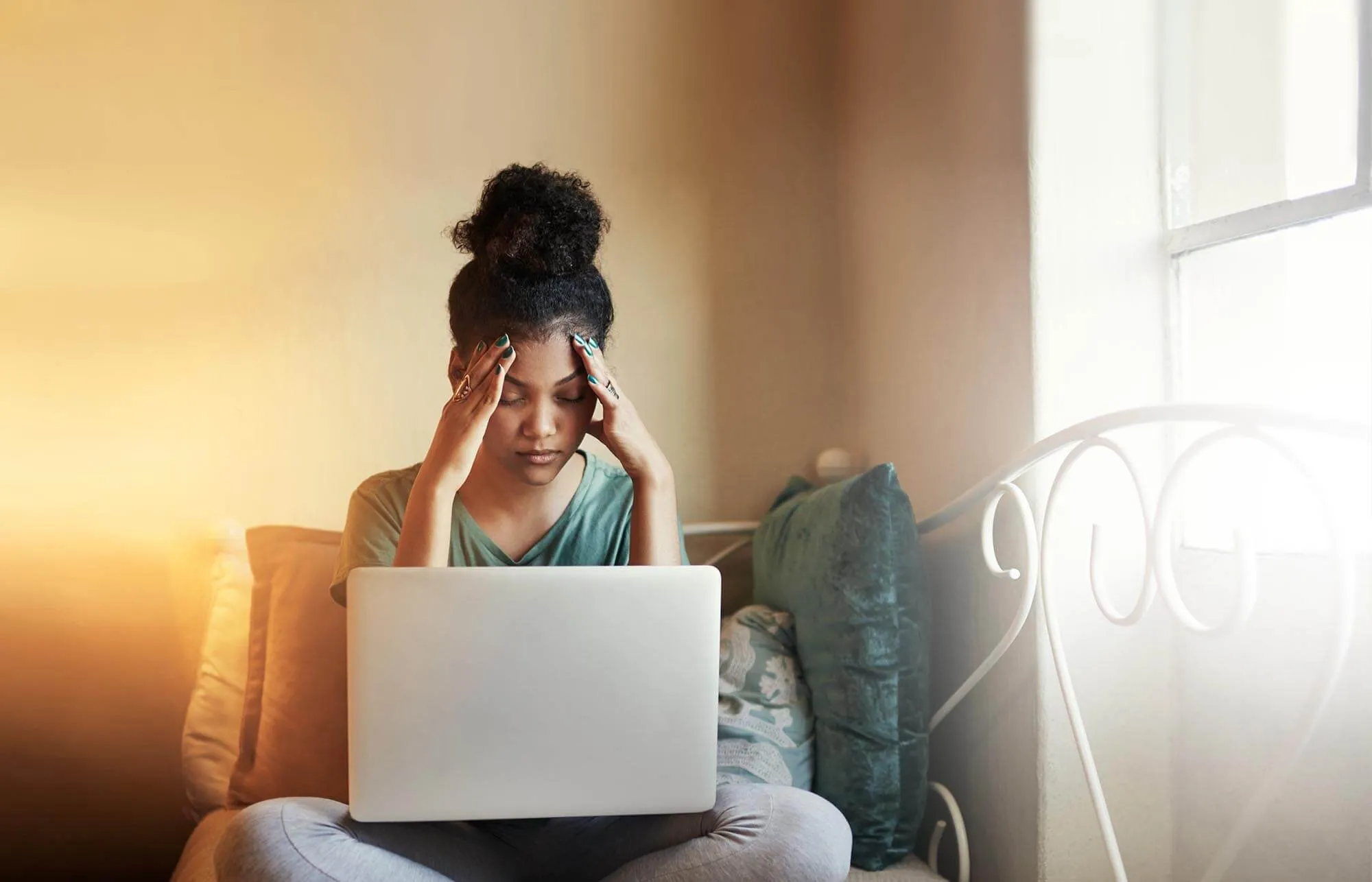 Tired young woman sitting cross-legged on a sofa with an open laptop