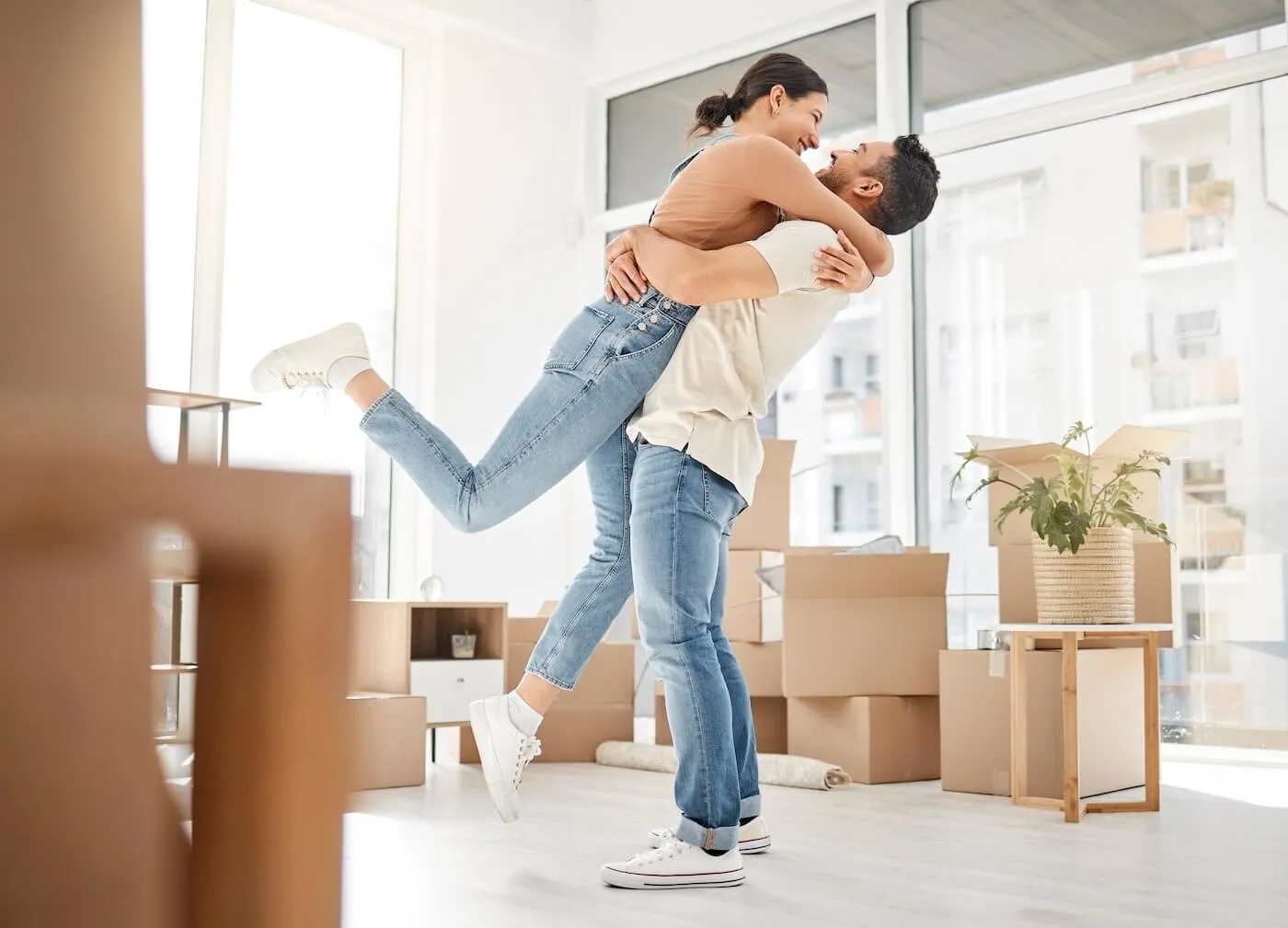 Happy couple hugging each other in the middle of the room, surrounded by moving boxes