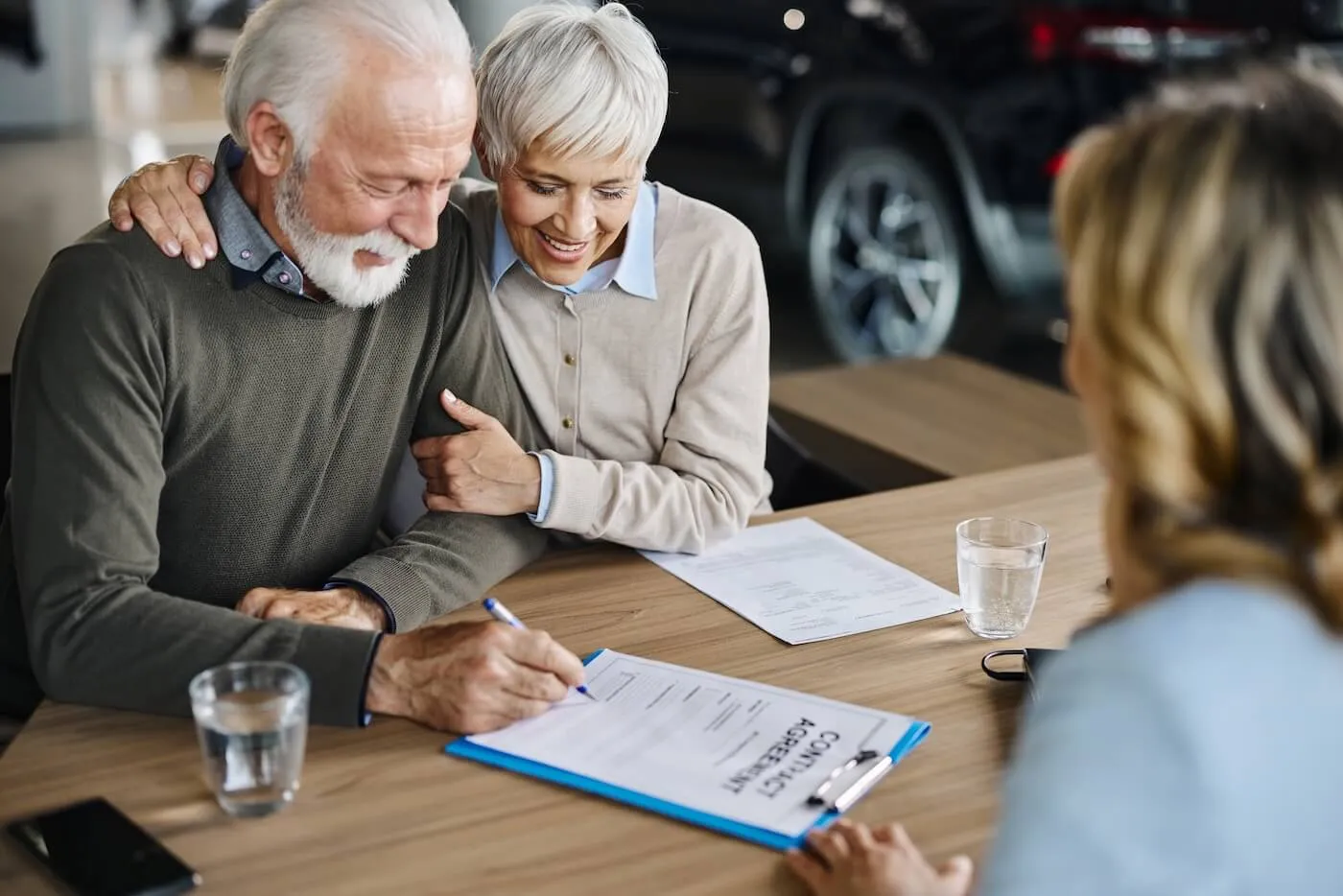 Happy senior couple signing a contract in the car dealership