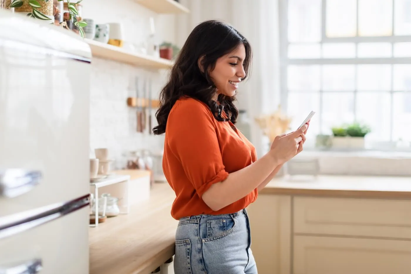 Smiling young woman checking her phone in the kitchen