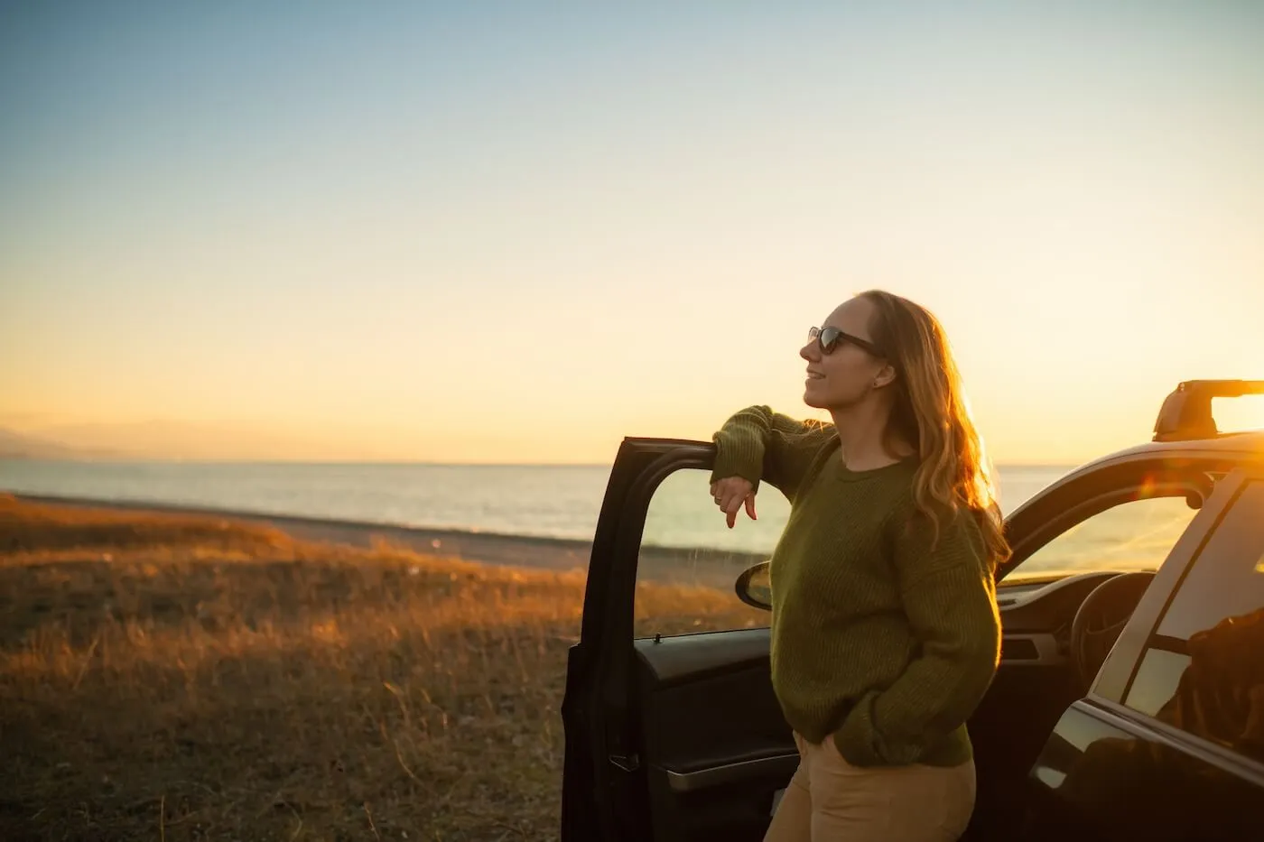 Woman enjoying sunset over the sea on the beach near her car