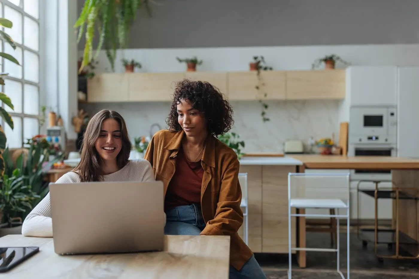 Two female flatmates sitting in a cozy kitchen and sharing a laptop