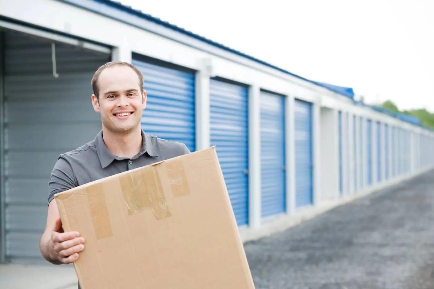Smiling man standing next to the storage units and holding a moving box