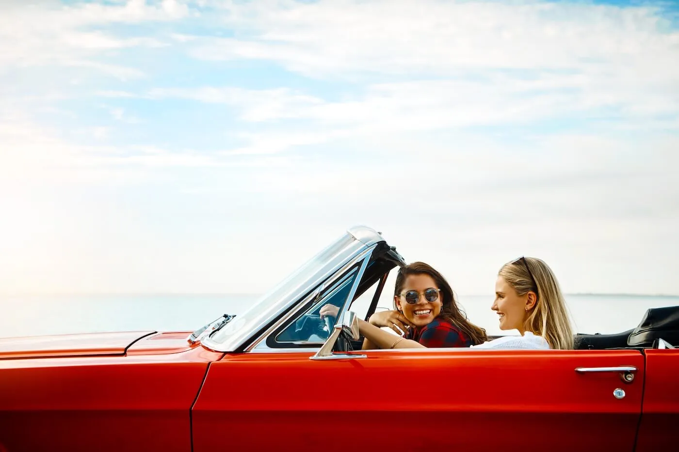 Two happy female friends driving a red convertible on the beach