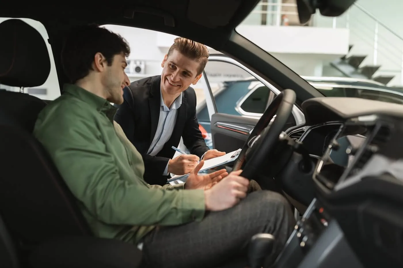 Man is sitting in the new car and talking to a male dealership agent