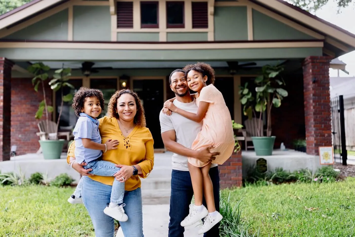 Happy family with two kids making a photo in front of their house, parents holding the kids