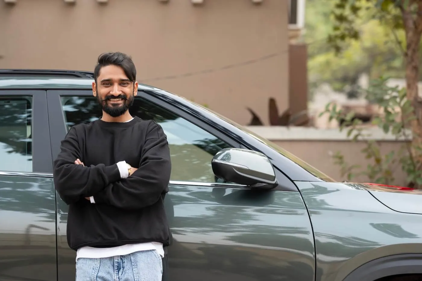 Smiling young man in the relaxed outfit posing for a photo next to his new car