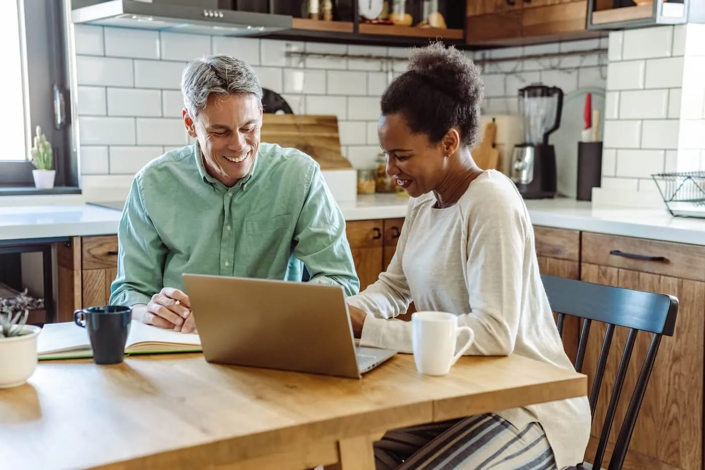 A mature couple sitting at their kitchen table, reviewing financial documents and using a laptop to plan their finances together.
