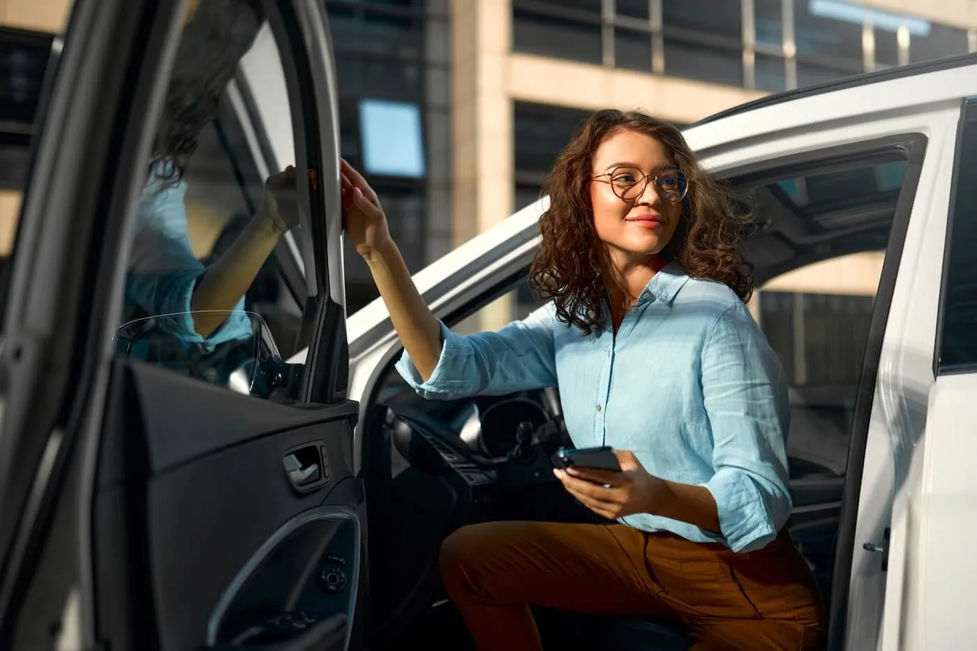 Young business woman getting out of the car while holding her smartphone.