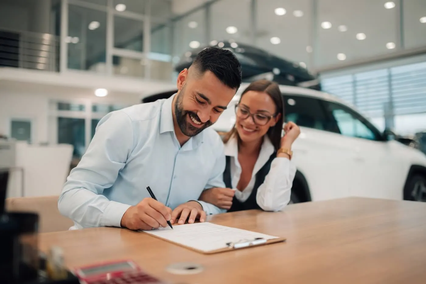 Happy couple signing papers for the car loan in a dealership