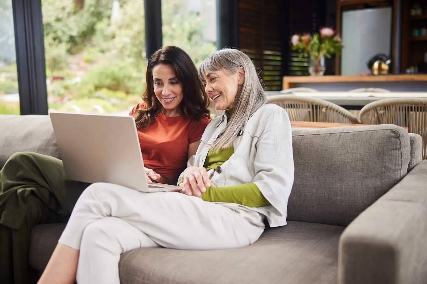 Smiling woman sitting on a sofa with her senior mother and using a laptop