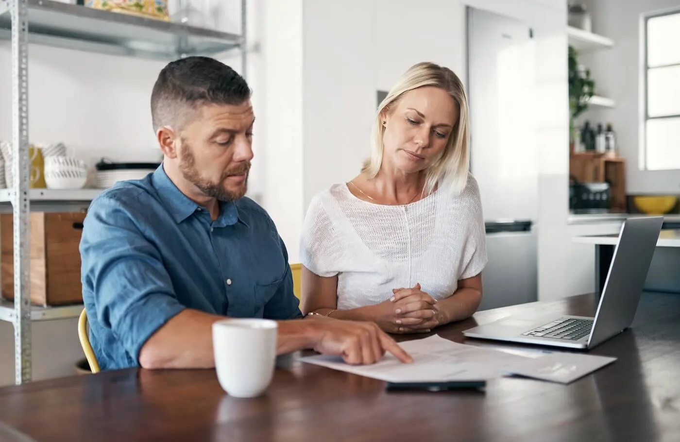 Mature couple sitting at a desk at home, attentively reviewing a document together, with a laptop open and a coffee mug nearby
