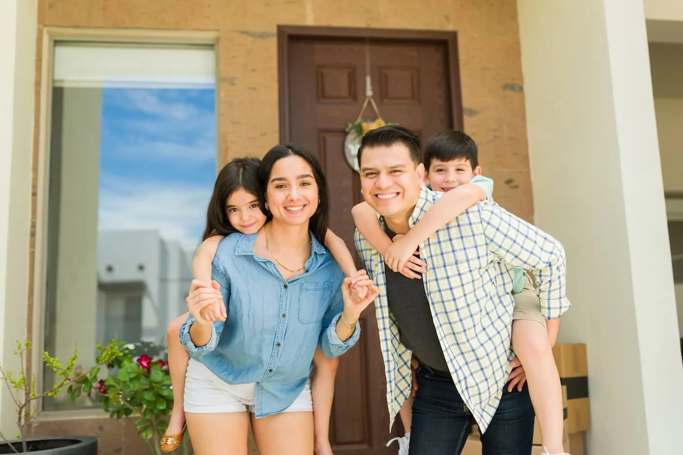 Happy mom and dad piggybacking their kids having fun in the entryway while moving into a new house