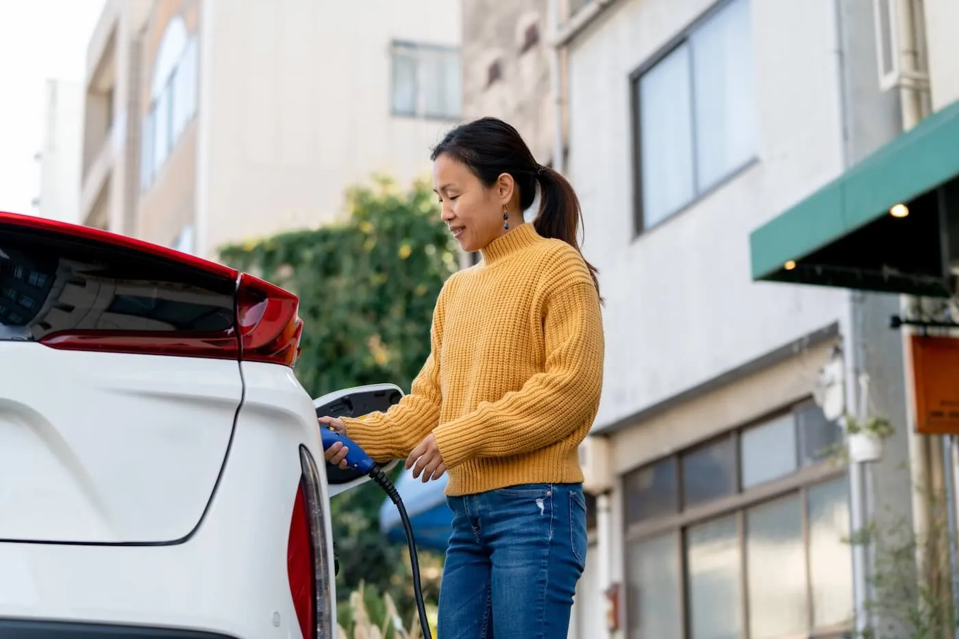 Smiling mature woman charging her EV on the street parking