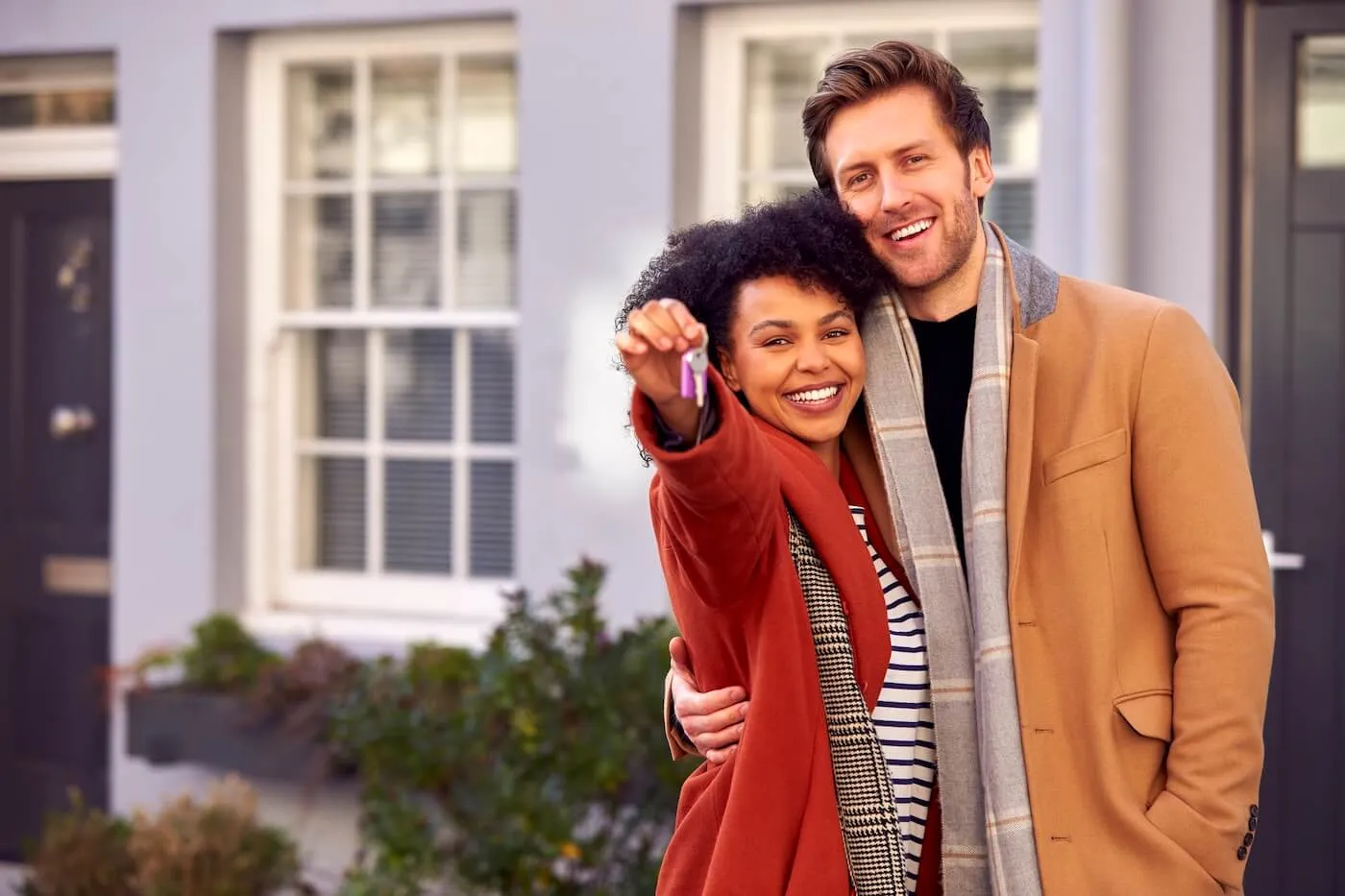 Happy couple standing next to their new house and holding the keys