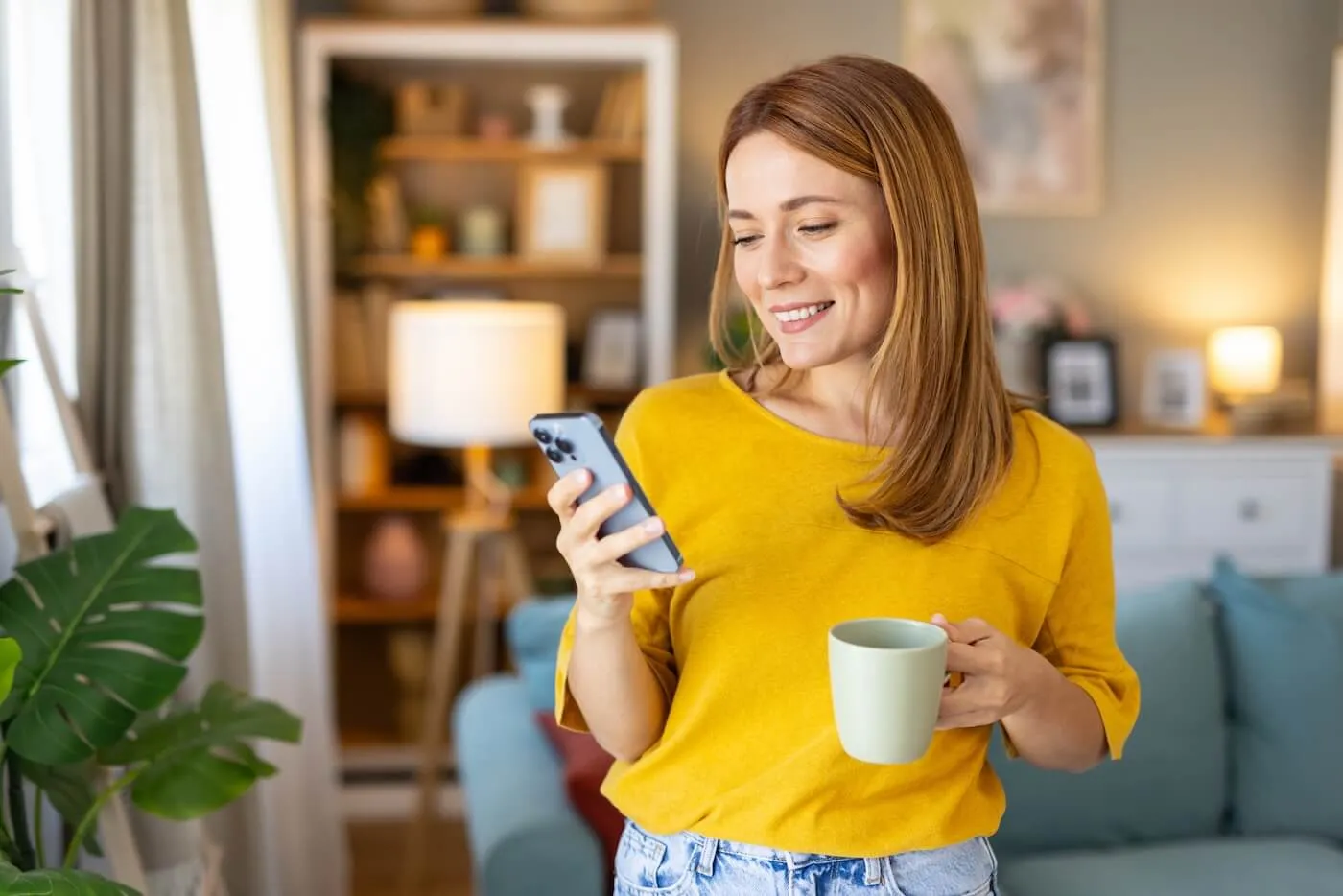 Smiling woman enjoying coffee while checking her savings account on the smartphone