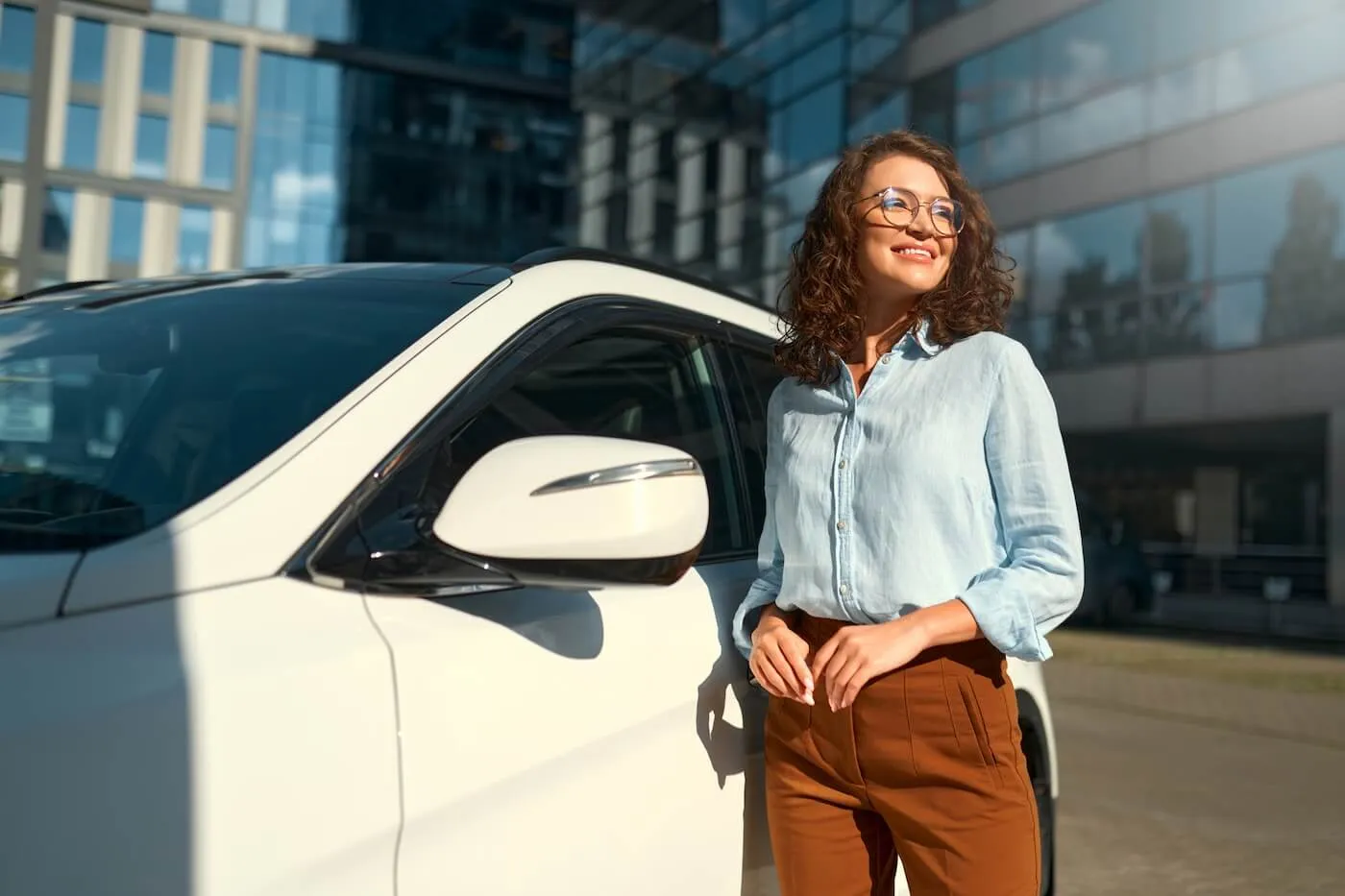 Smiling young woman standing next to a white car near the office building