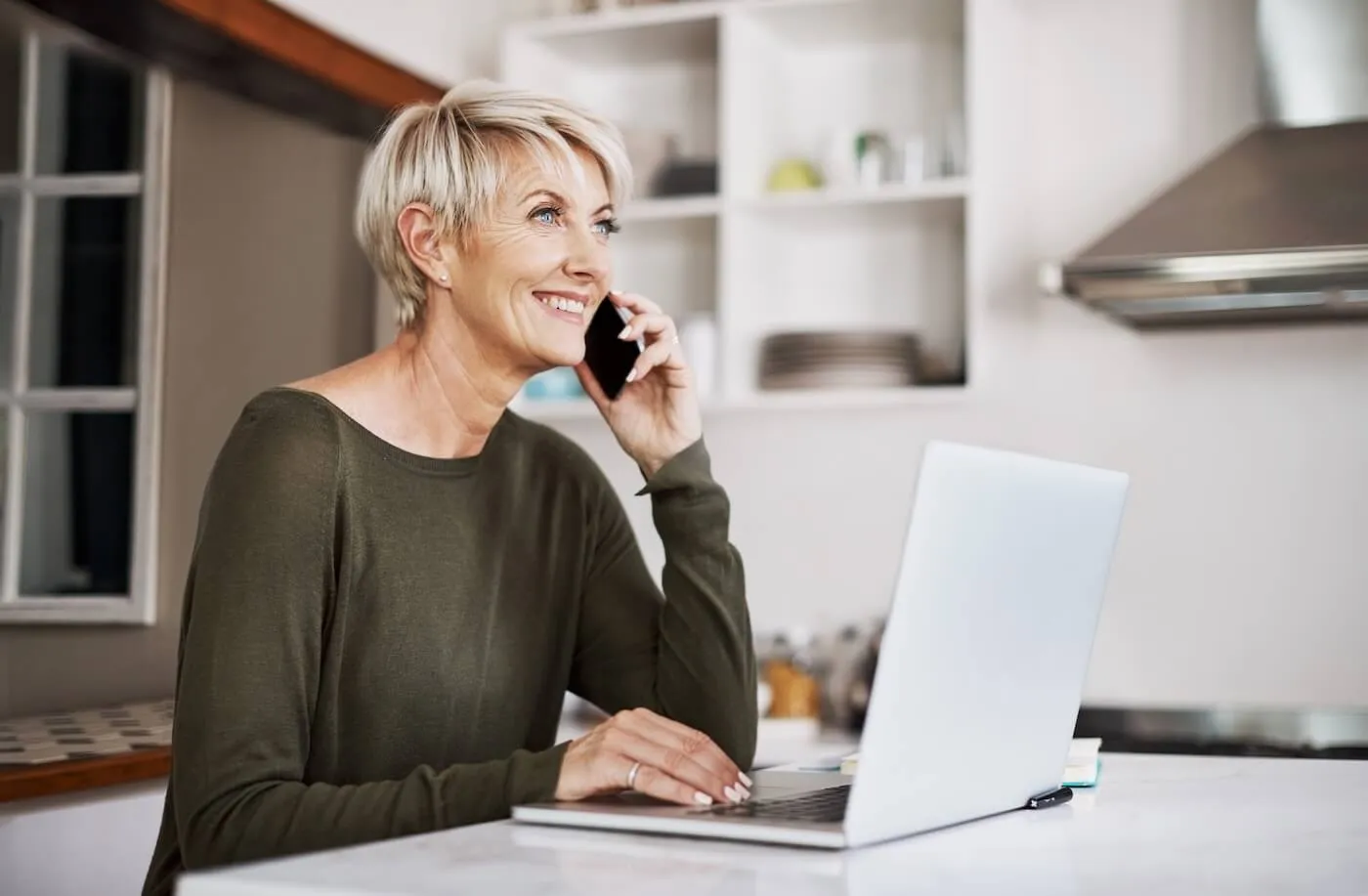 Smiling senior woman making a phone call while working on her laptop from home