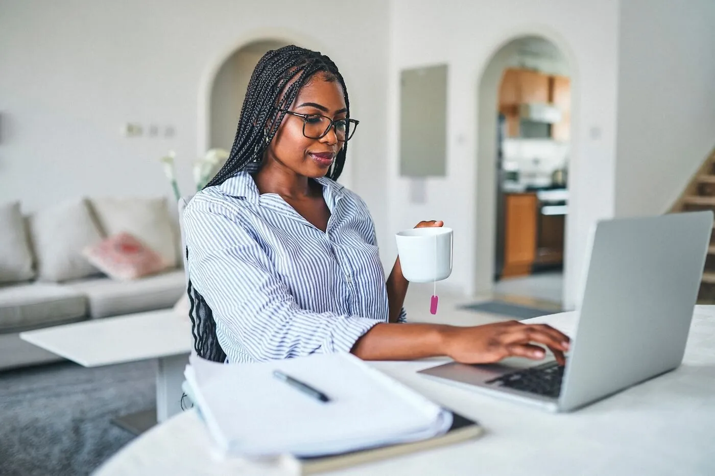Young woman working on a laptop in a home office while enjoying a cup of tea