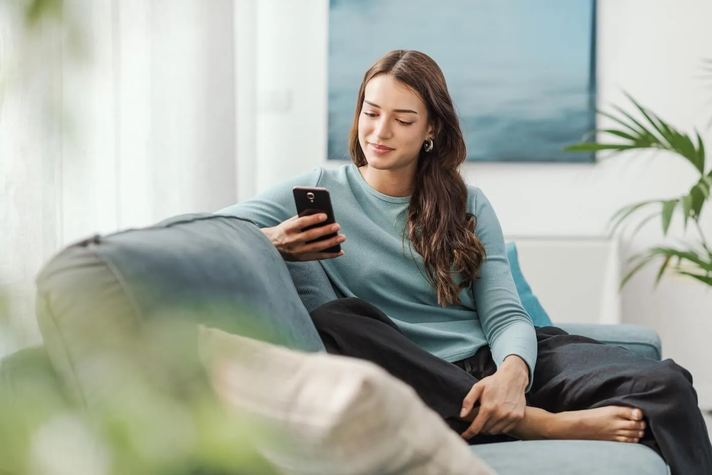 Young woman sitting comfortably on a couch and using her smartphone
