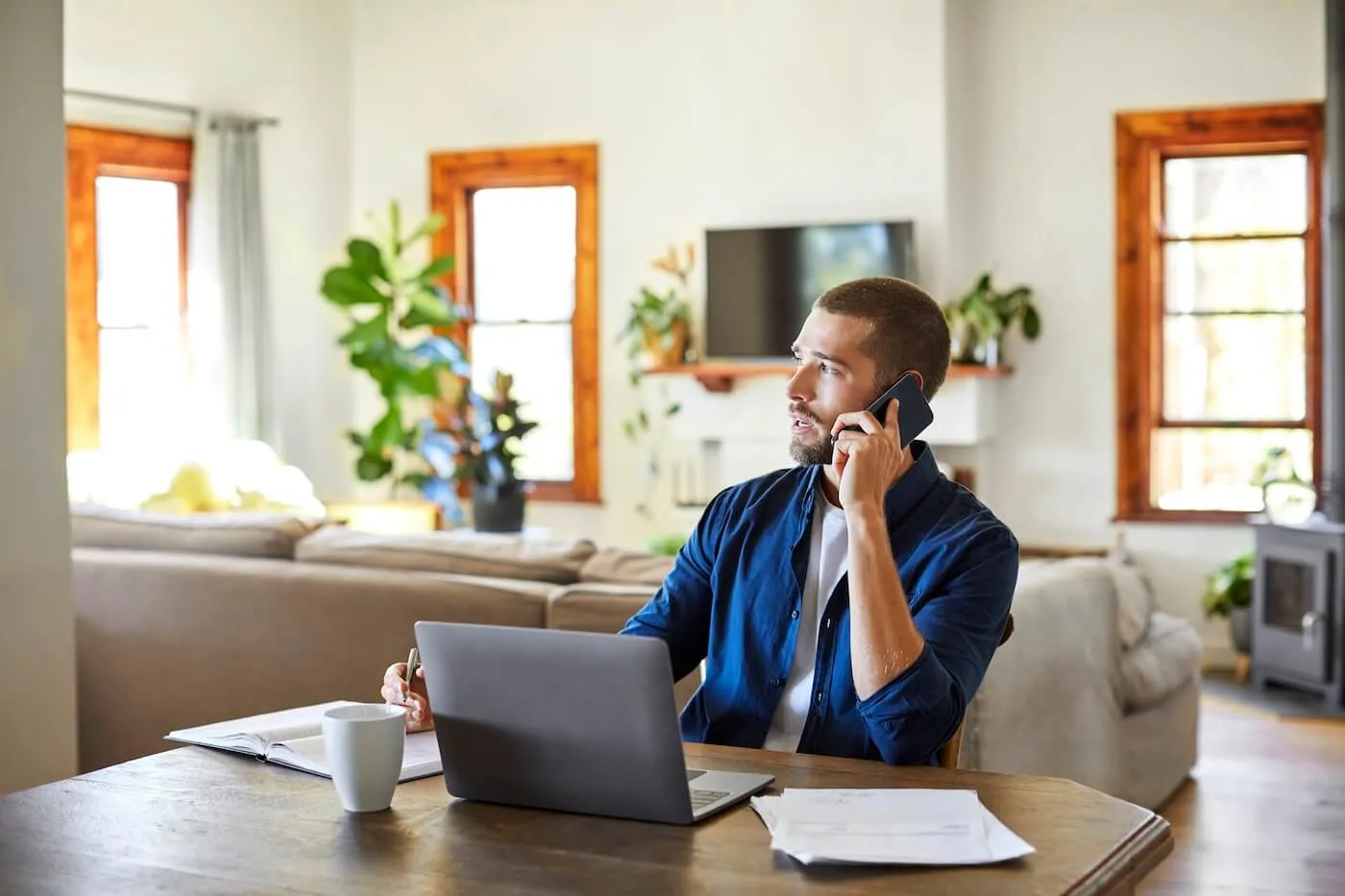 Male tenant in a home office, making a phone call to his rental insurance provider, with documents and a laptop on the desk