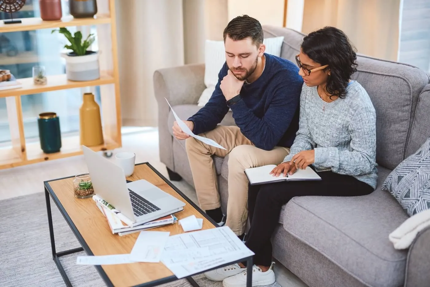 Focused young couple discussing their finances at home, with a laptop and printouts beside them