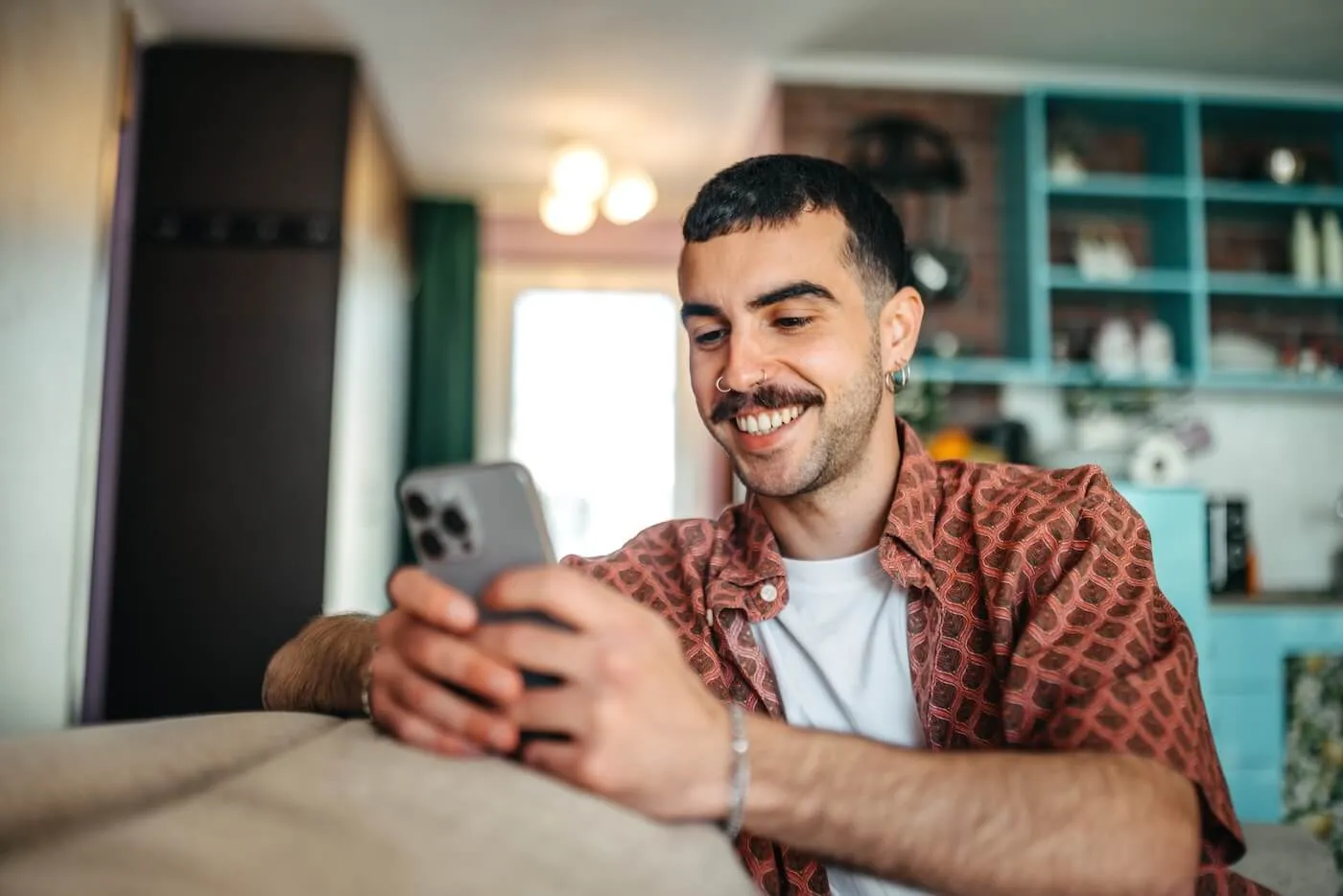 Smiling young man with a face piercing checking his smartphone at home.