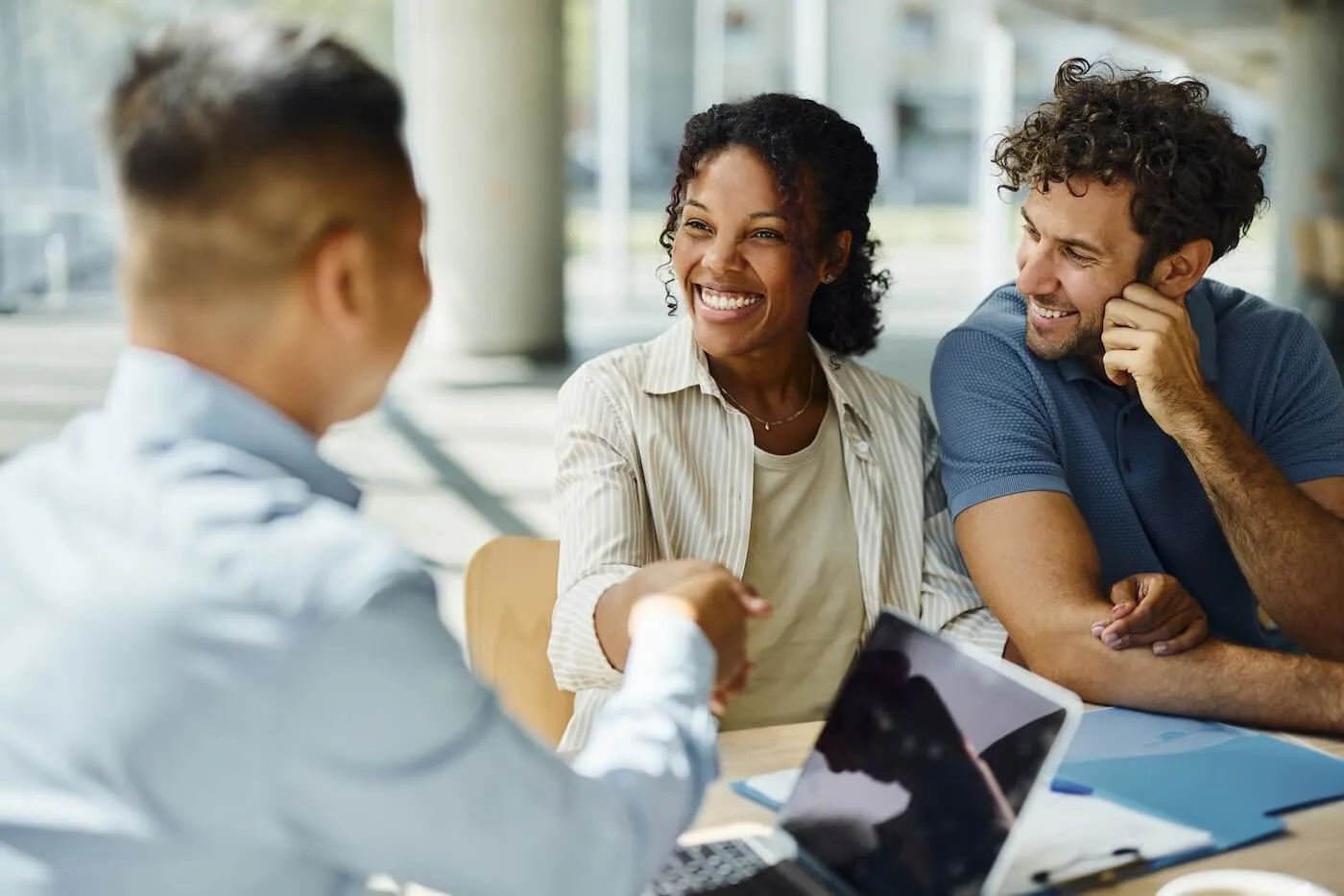 Smiling young woman is shaking hands with a male financial adviser, a happy man seating beside her.